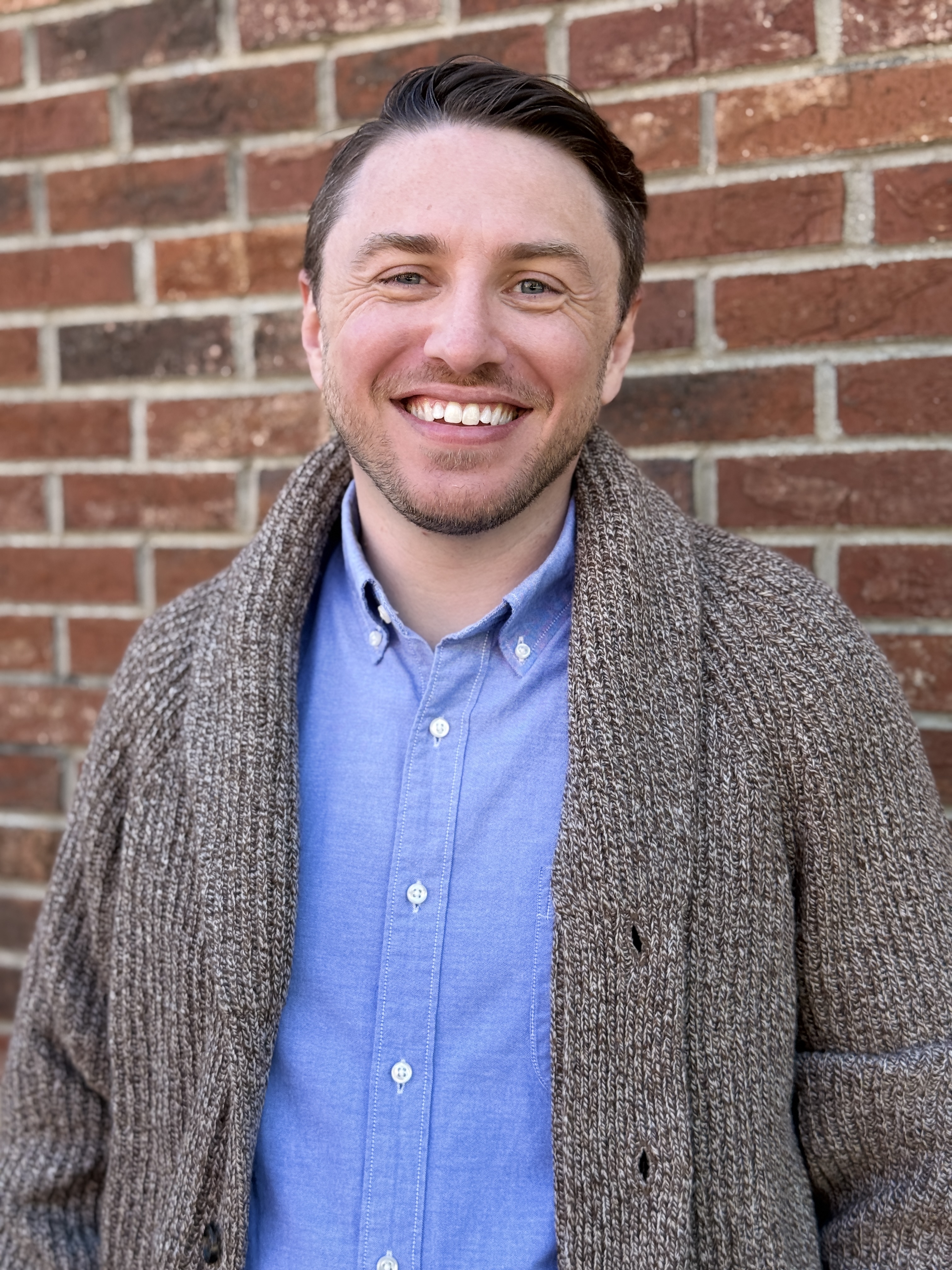 Dr. Aaron Miller, Ph.D., smiling against a brick wall backdrop